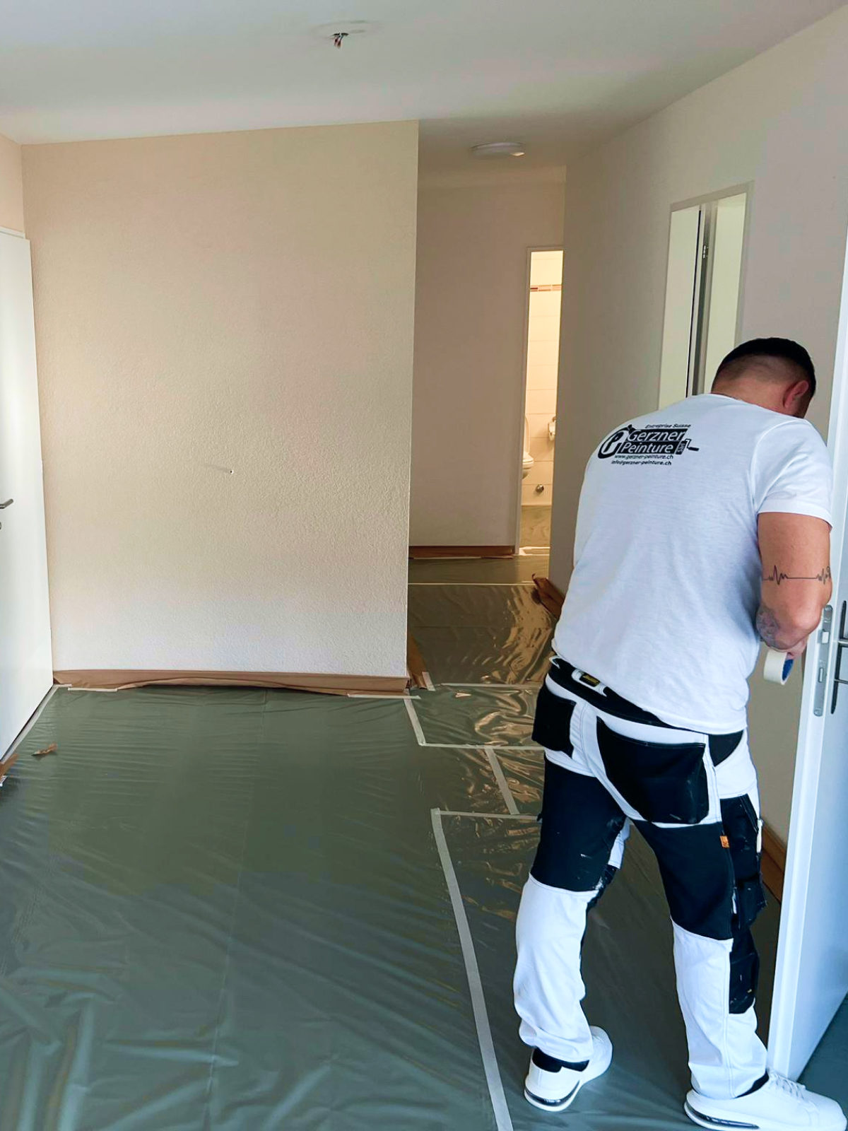 Un homme protège une porte pour ensuite peindre les murs en blanc dans un appartement à Vevey.